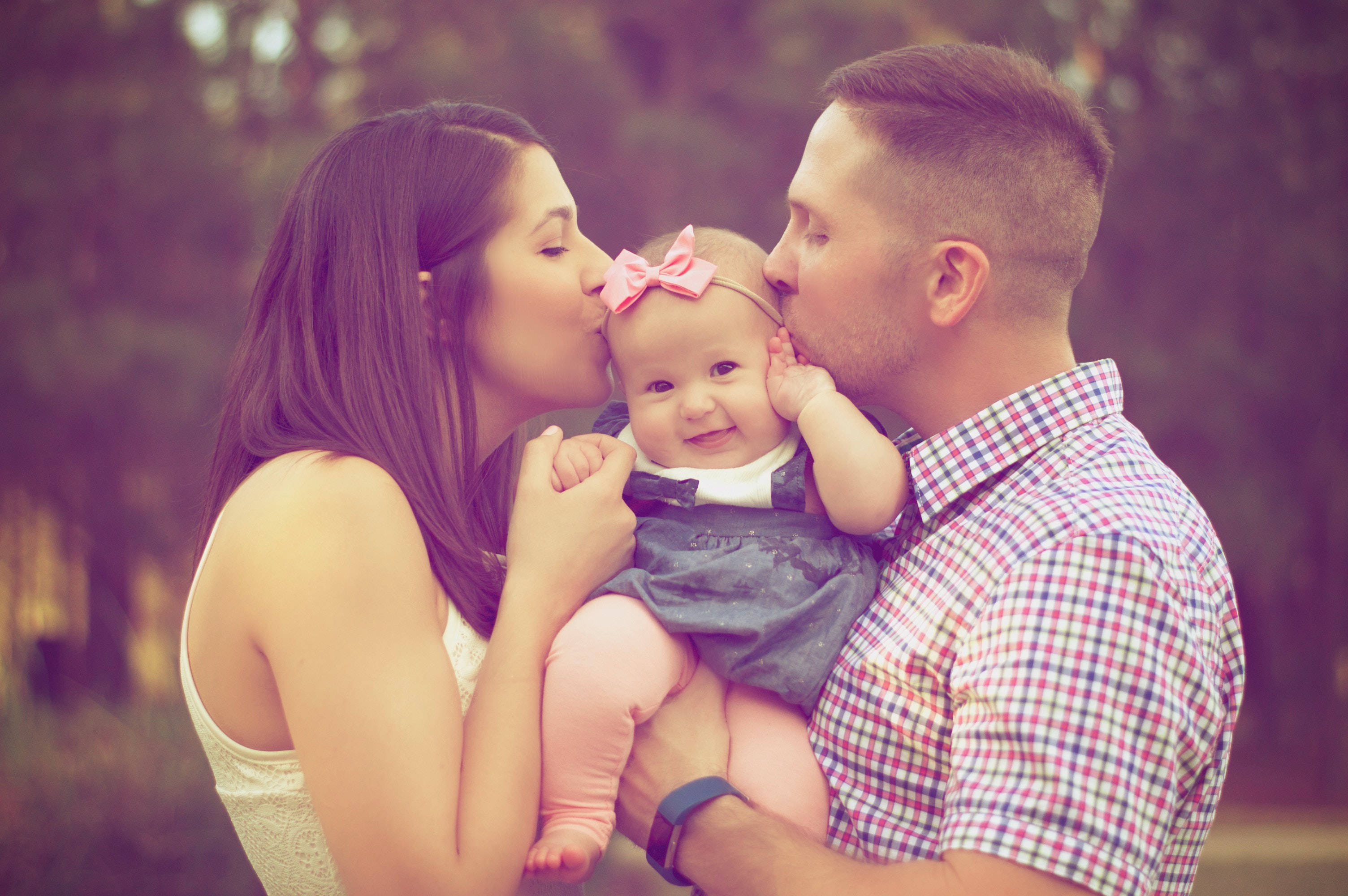Couple holding and kissing their baby after successful IUI fertility treatment at our Kingwood and The Woodlands fertility clinics