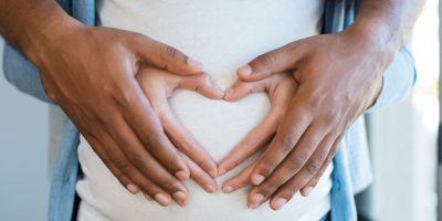 Husband and wife holding hands over pregnant belly after successful fertility treatment at our North Houston IVF clinic in the woodlands and Kingwood