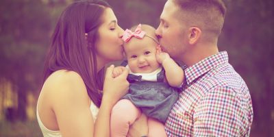 Couple holding and kissing their baby after successful IUI fertility treatment at our Kingwood and The Woodlands fertility clinics