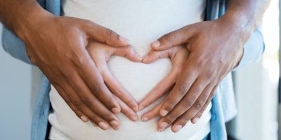Husband and wife holding hands over pregnant belly after successful fertility treatment at our North Houston IVF clinic in the woodlands and Kingwood